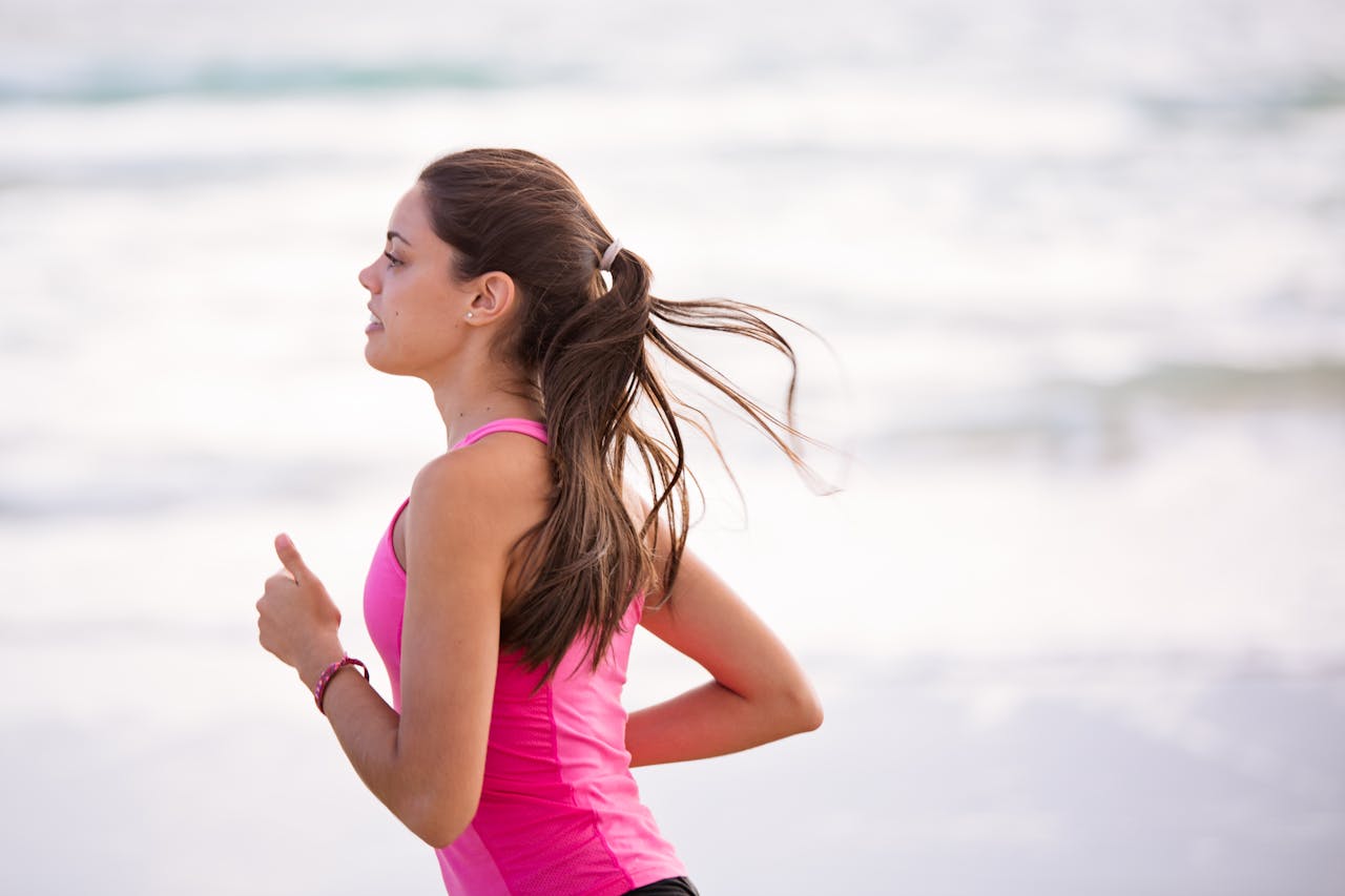 Side view of a young woman jogging on a beach wearing pink active wear.